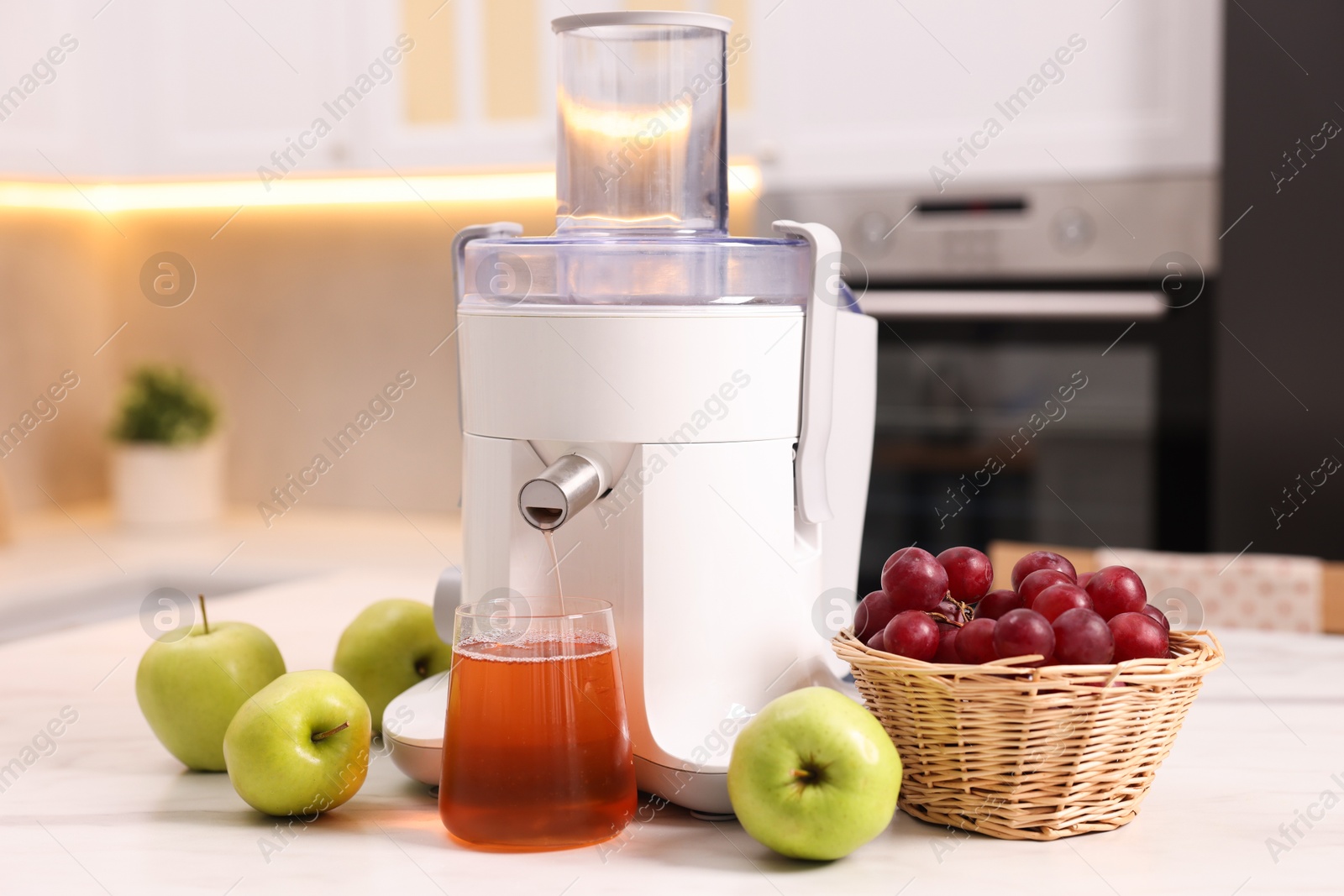 Photo of Modern juicer, fresh fruits and glass on white marble table in kitchen