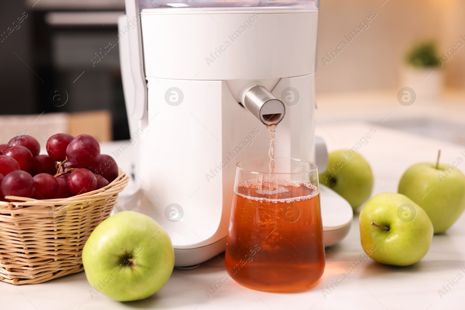 Photo of Modern juicer, fresh fruits and glass on white marble table in kitchen, closeup