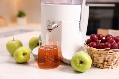 Photo of Modern juicer, fresh fruits and glass on white marble table in kitchen, closeup