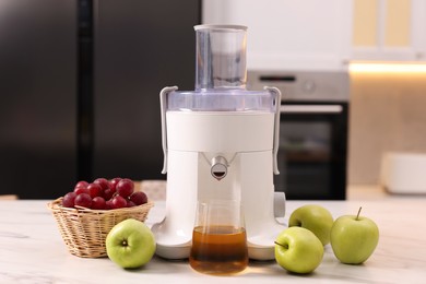 Photo of Modern juicer, fresh fruits and glass on white marble table in kitchen