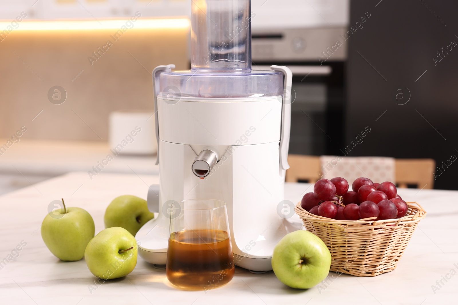 Photo of Modern juicer, fresh fruits and glass on white marble table in kitchen