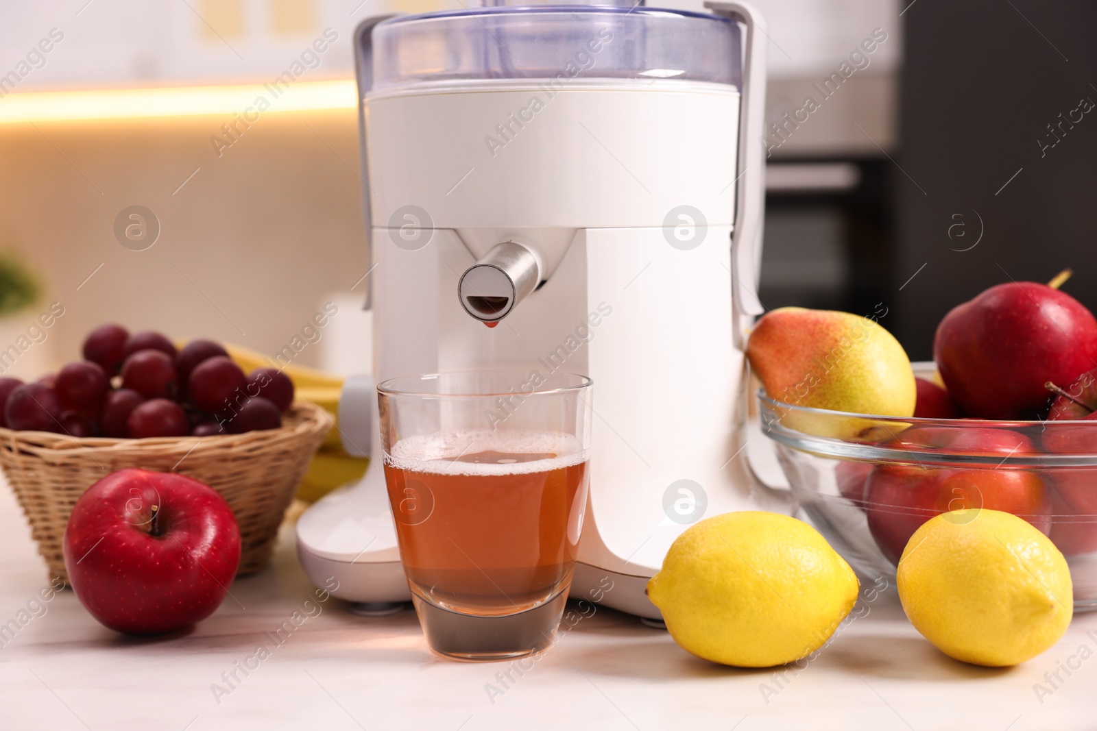 Photo of Modern juicer, fresh fruits and glass on white marble table in kitchen, closeup