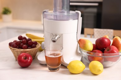 Photo of Modern juicer, fresh fruits and glass on white marble table in kitchen