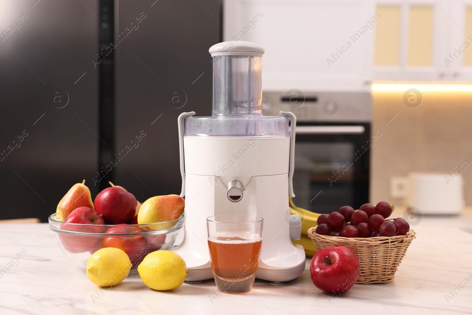 Photo of Modern juicer, fresh fruits and glass on white marble table in kitchen