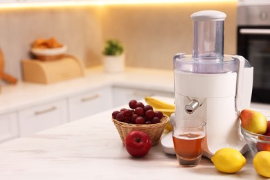 Photo of Modern juicer, fresh fruits and glass on white marble table in kitchen, space for text