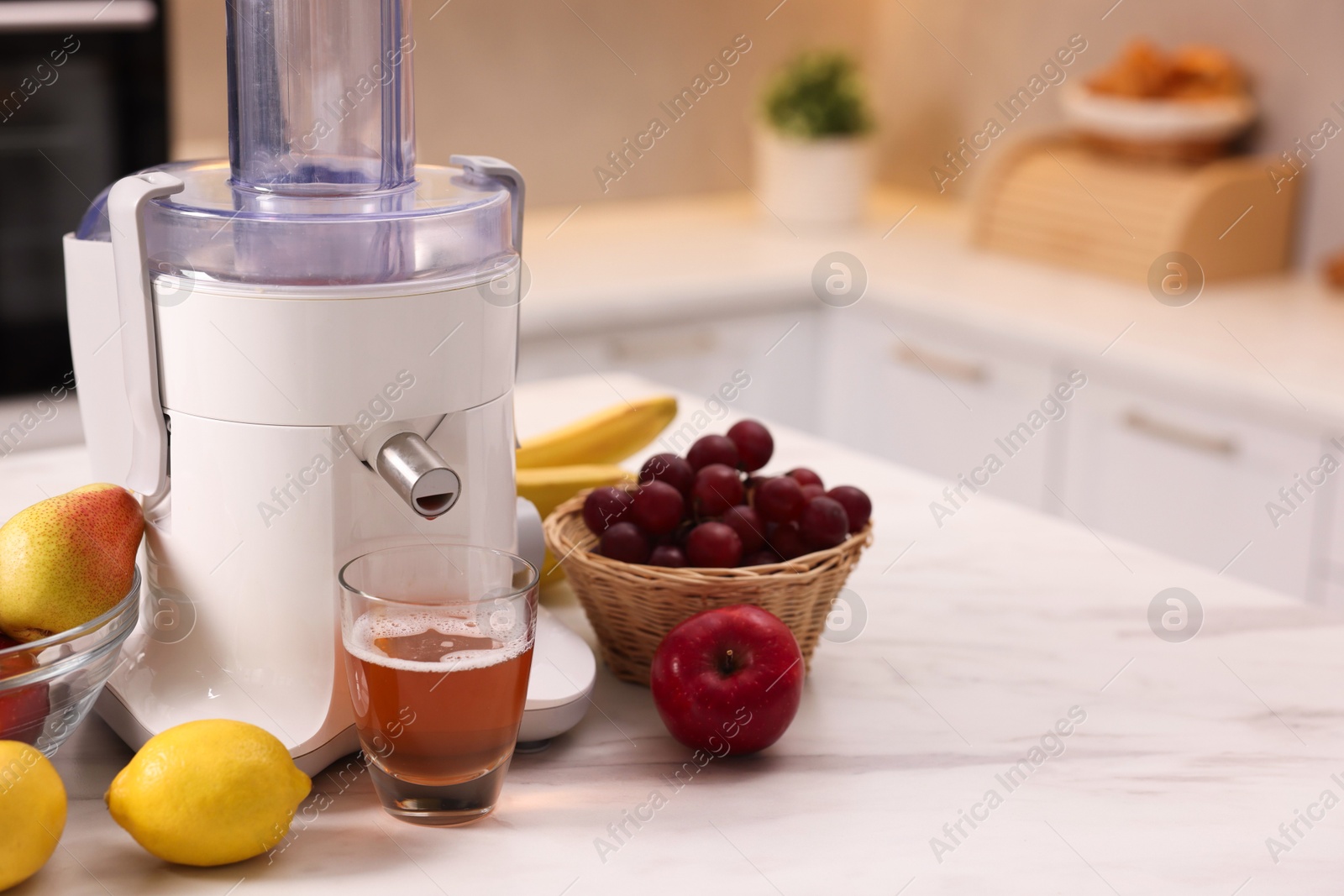 Photo of Modern juicer, fresh fruits and glass on white marble table in kitchen, space for text