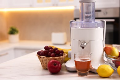 Photo of Modern juicer, fresh fruits and glass on white marble table in kitchen