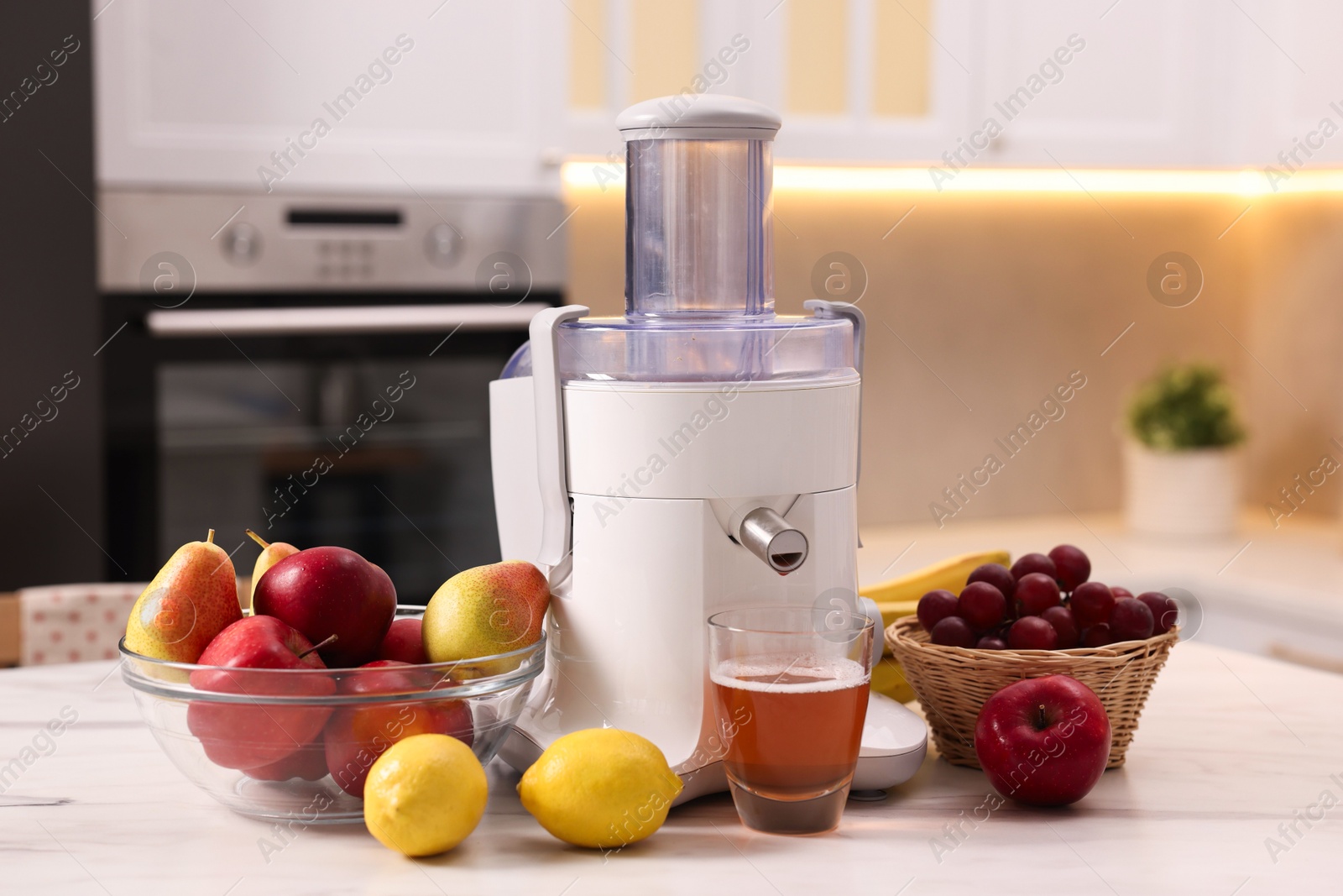 Photo of Modern juicer, fresh fruits and glass on white marble table in kitchen