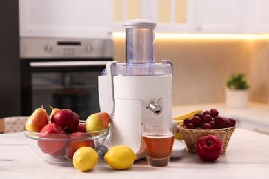 Photo of Modern juicer, fresh fruits and glass on white marble table in kitchen