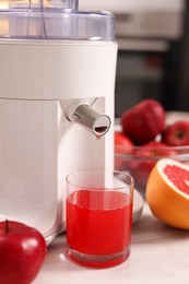 Photo of Modern juicer, fresh fruits and glass on white marble table in kitchen, closeup