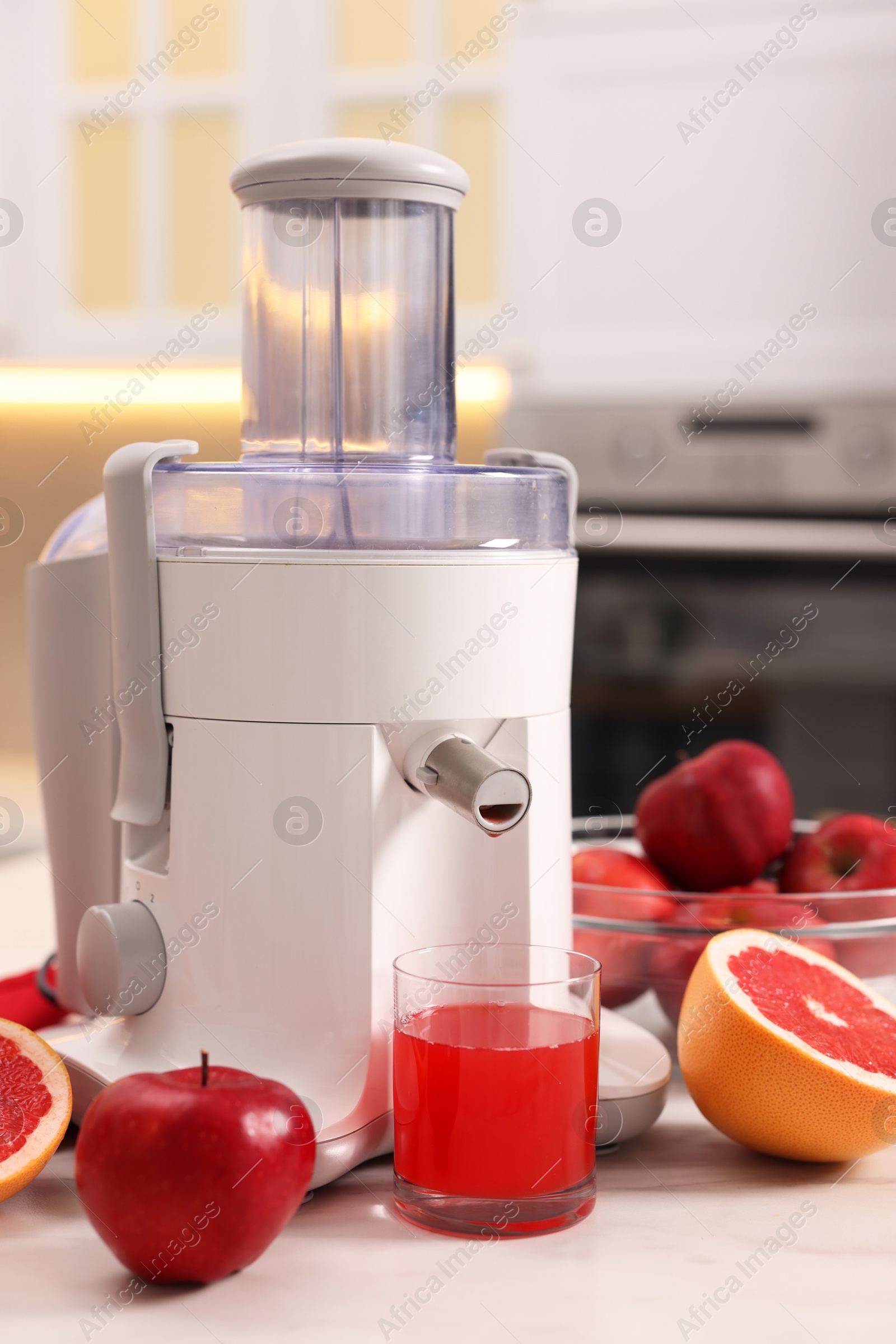 Photo of Modern juicer, fresh fruits and glass on white marble table in kitchen