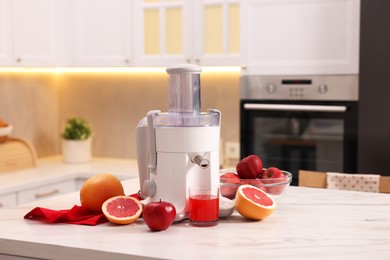 Photo of Modern juicer, fresh fruits and glass on white marble table in kitchen