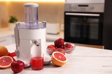 Photo of Modern juicer, fresh fruits and glass on white marble table in kitchen