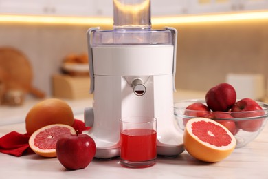 Photo of Modern juicer, fresh fruits and glass on white marble table in kitchen