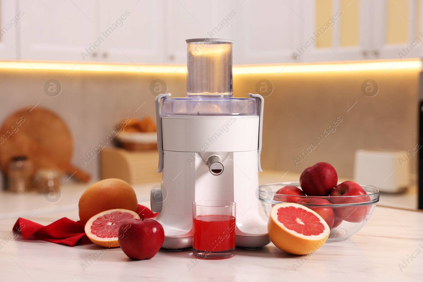 Photo of Modern juicer, fresh fruits and glass on white marble table in kitchen