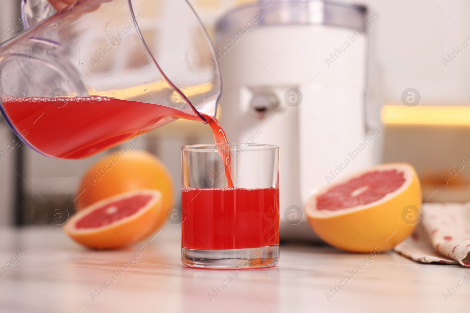 Photo of Pouring tasty grapefruit juice into glass at white marble table in kitchen, closeup