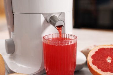 Photo of Modern juicer, fresh grapefruit and glass on table in kitchen, closeup