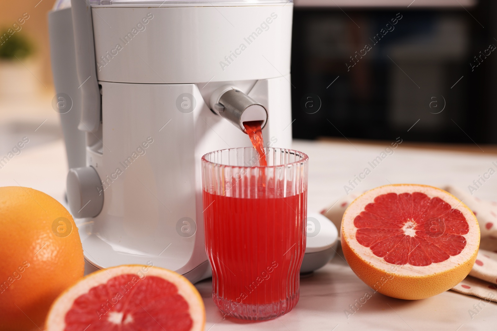 Photo of Modern juicer, fresh grapefruits and glass on white marble table in kitchen, closeup