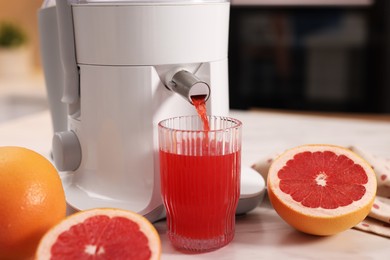 Photo of Modern juicer, fresh grapefruits and glass on white marble table in kitchen, closeup