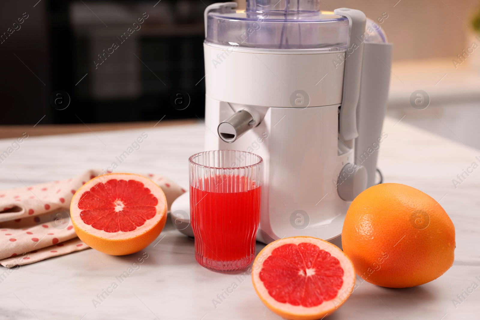 Photo of Modern juicer, fresh grapefruits and glass on white marble table in kitchen