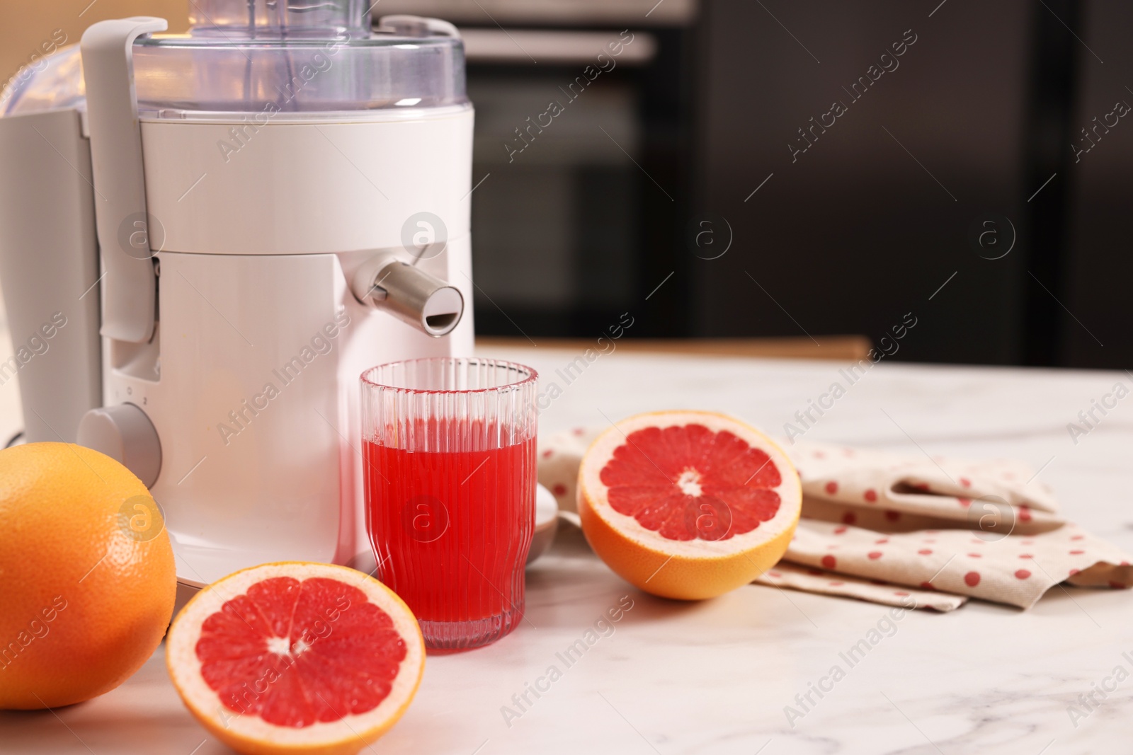 Photo of Modern juicer, fresh grapefruits and glass on white marble table in kitchen