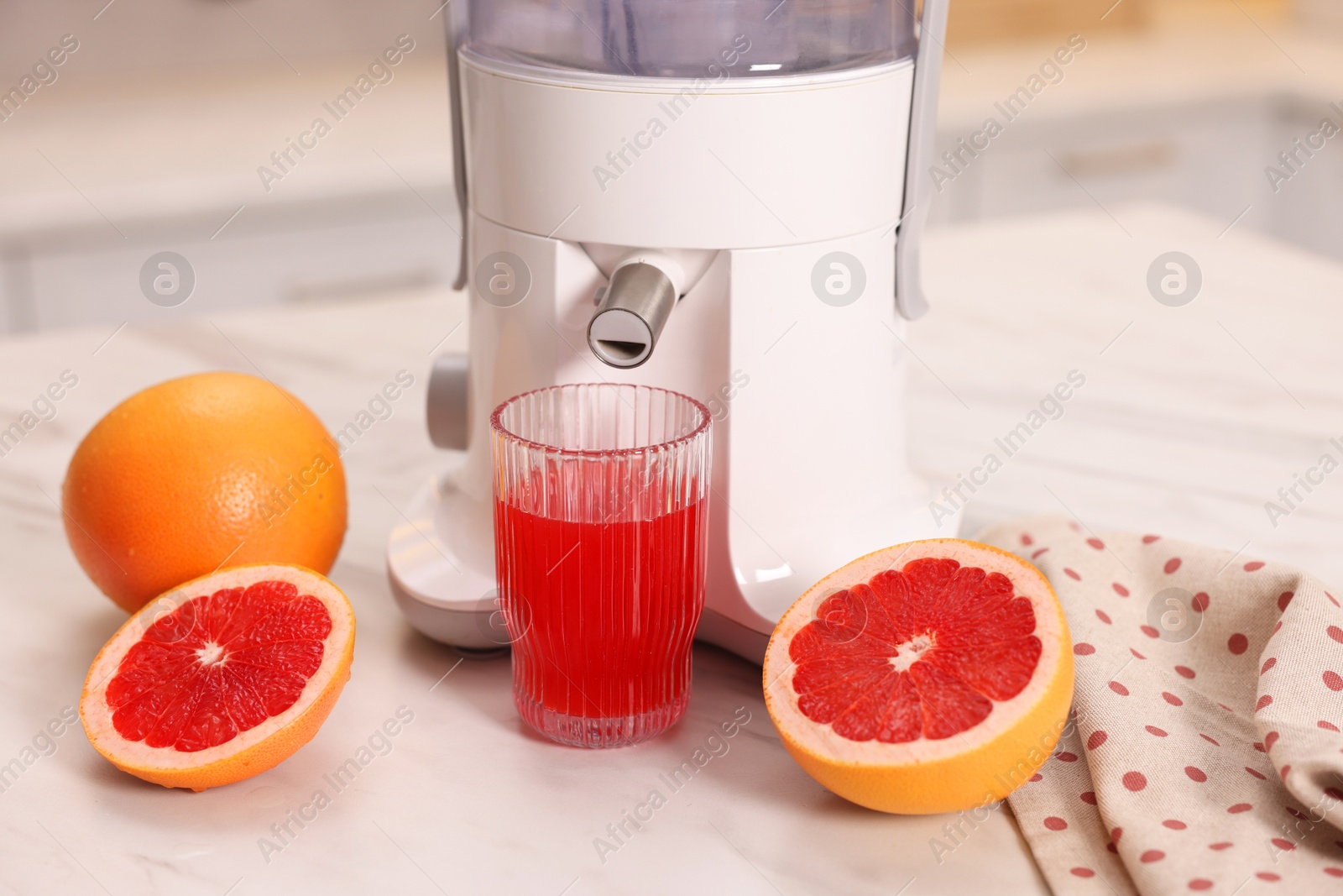 Photo of Modern juicer, fresh grapefruits and glass on white marble table in kitchen