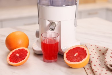 Photo of Modern juicer, fresh grapefruits and glass on white marble table in kitchen