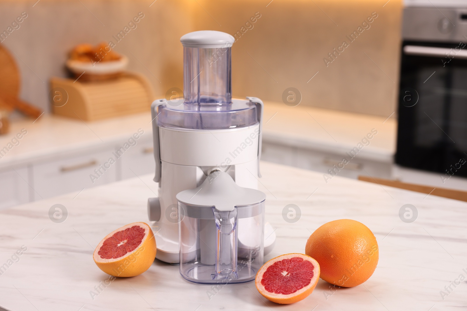 Photo of Modern juicer and fresh grapefruits on white marble table in kitchen