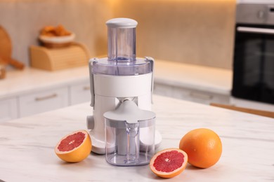 Photo of Modern juicer and fresh grapefruits on white marble table in kitchen