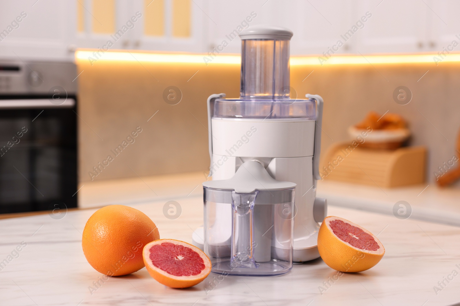 Photo of Modern juicer and fresh grapefruits on white marble table in kitchen