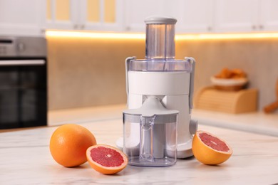 Photo of Modern juicer and fresh grapefruits on white marble table in kitchen