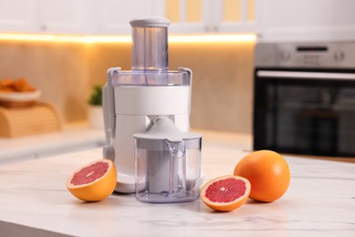 Photo of Modern juicer and fresh grapefruits on white marble table in kitchen