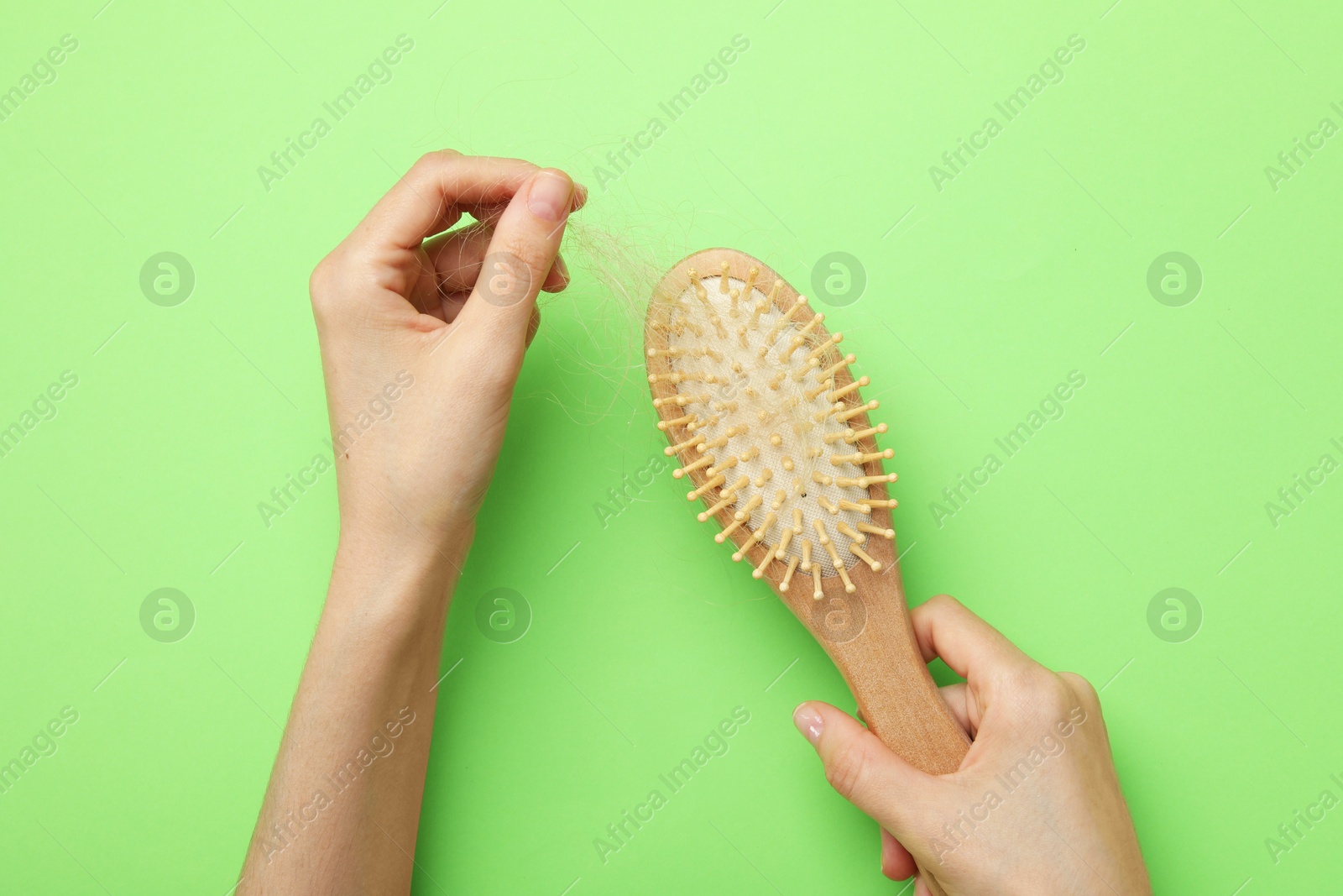 Photo of Woman taking her lost hair from brush on light green background, top view