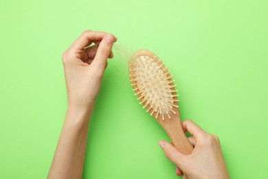 Woman taking her lost hair from brush on light green background, top view