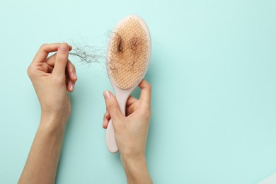 Woman taking her lost hair from brush on light blue background, top view. Space for text