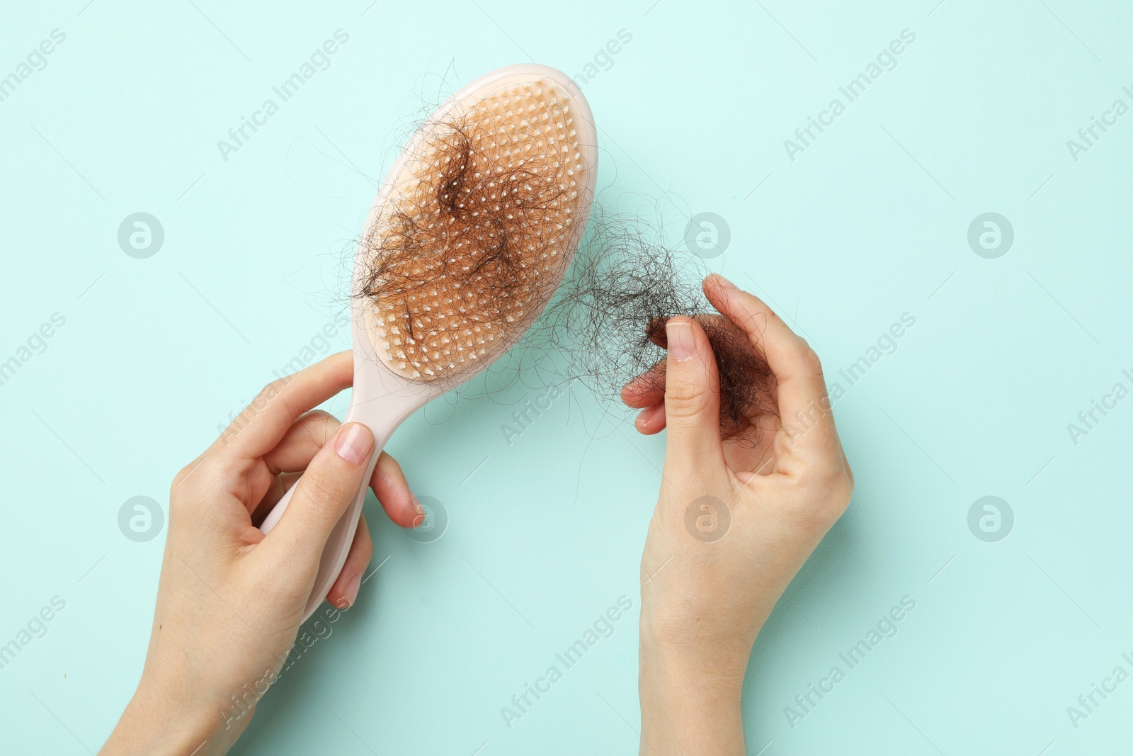 Photo of Woman taking her lost hair from brush on light blue background, top view. Alopecia problem