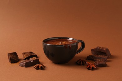 Tasty melted chocolate in cup and anise stars on brown background