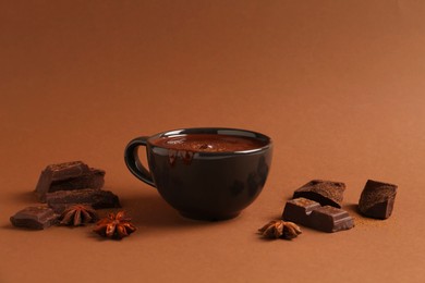 Photo of Tasty melted chocolate in cup and anise stars on brown background