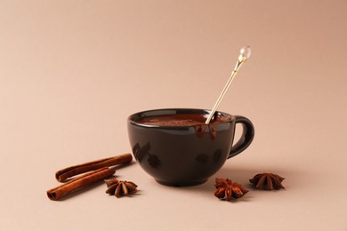 Photo of Tasty melted chocolate in cup, cinnamon sticks and anise stars on beige background