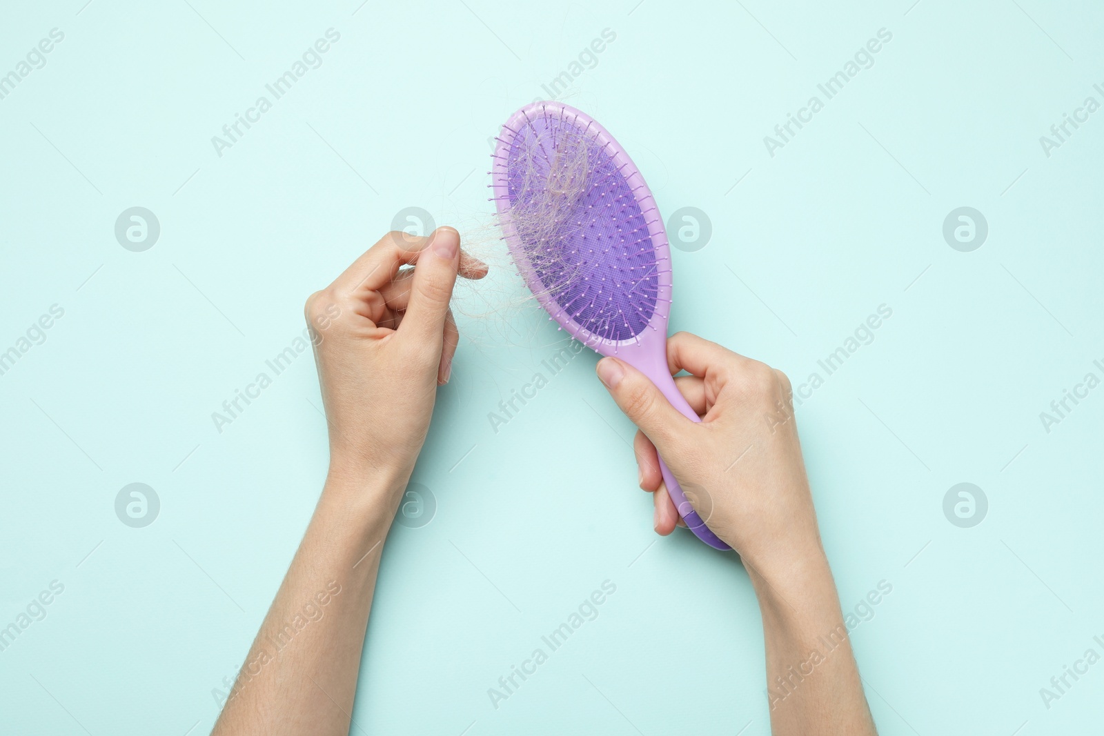 Photo of Woman taking her lost hair from brush on light blue background, top view. Alopecia problem