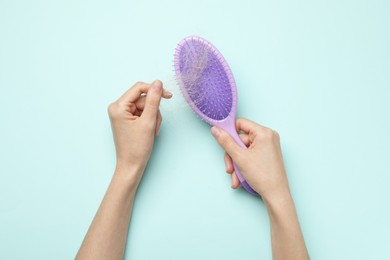 Woman taking her lost hair from brush on light blue background, top view. Alopecia problem