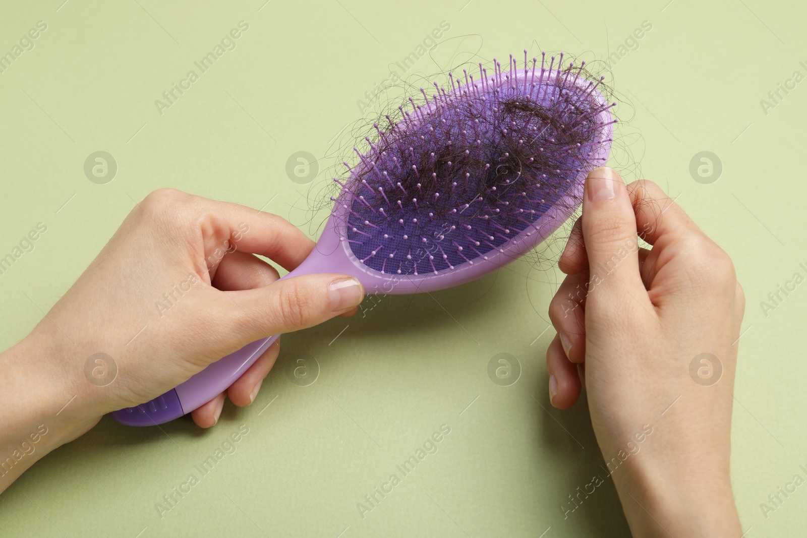 Photo of Woman taking her lost hair from brush on light olive background, closeup. Alopecia problem