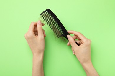 Photo of Woman taking her lost hair from comb on light green background, top view. Alopecia problem