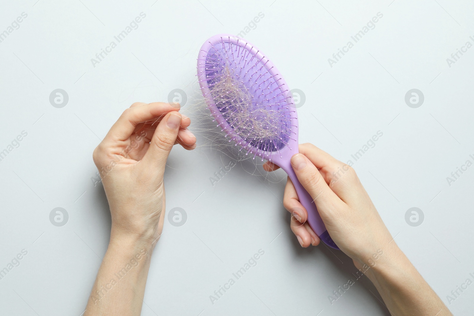 Photo of Woman taking her lost hair from brush on grey background, top view. Alopecia problem