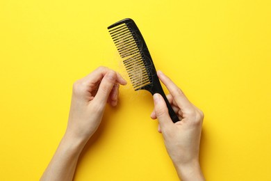 Photo of Woman taking her lost hair from comb on yellow background, top view. Alopecia problem