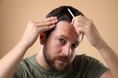 Man brushing his hair on beige background. Alopecia problem