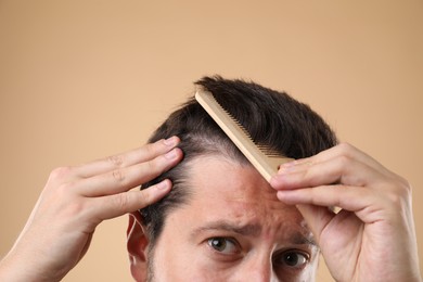 Photo of Man brushing his hair on beige background, closeup. Alopecia problem