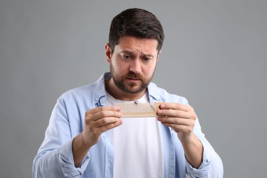 Sad man holding comb with lost hair on gray background. Alopecia problem