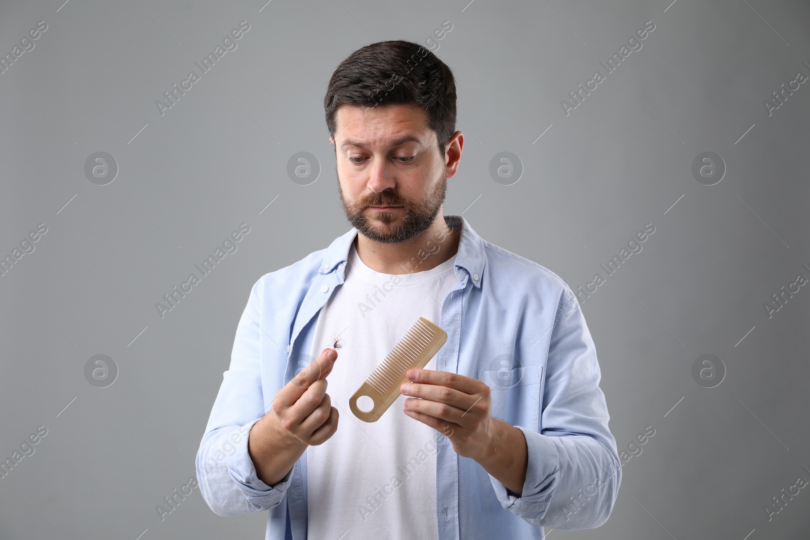 Photo of Sad man holding comb with lost hair on gray background. Alopecia problem