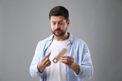 Sad man holding comb with lost hair on gray background. Alopecia problem